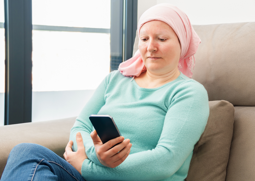 Woman with cancer looking at phone while getting treatment